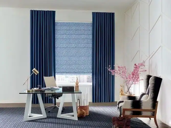 Bright workspace featuring blue drapes, a sleek desk, comfortable chair, and decorative pink flowers for a cozy, productive environment.