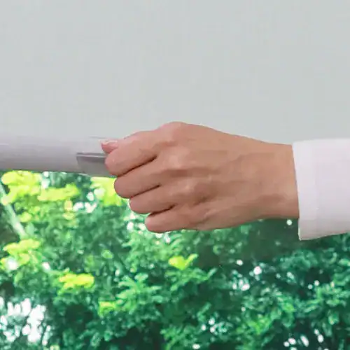 Close-up of a hand holding a garden spray bottle outdoors with green foliage background.
