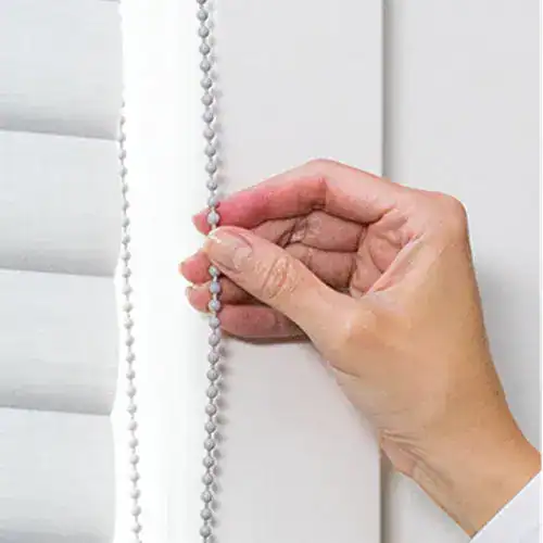 Close-up of hand adjusting a vertical cord for window blinds or shades. Focusing on window treatment and hand operation.