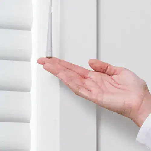 Close-up of a hand checking a white window blind with horizontal slats.