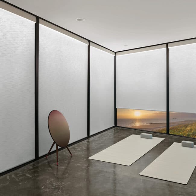 Bright modern yoga studio with large windows overlooking scenic beach sunset, minimalist decor, yoga mats, bolster cushions, and tranquil ambiance for relaxation and mindfulness.