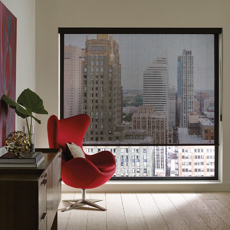 Modern city skyline visible through large window with roller shade in high-rise apartment.
