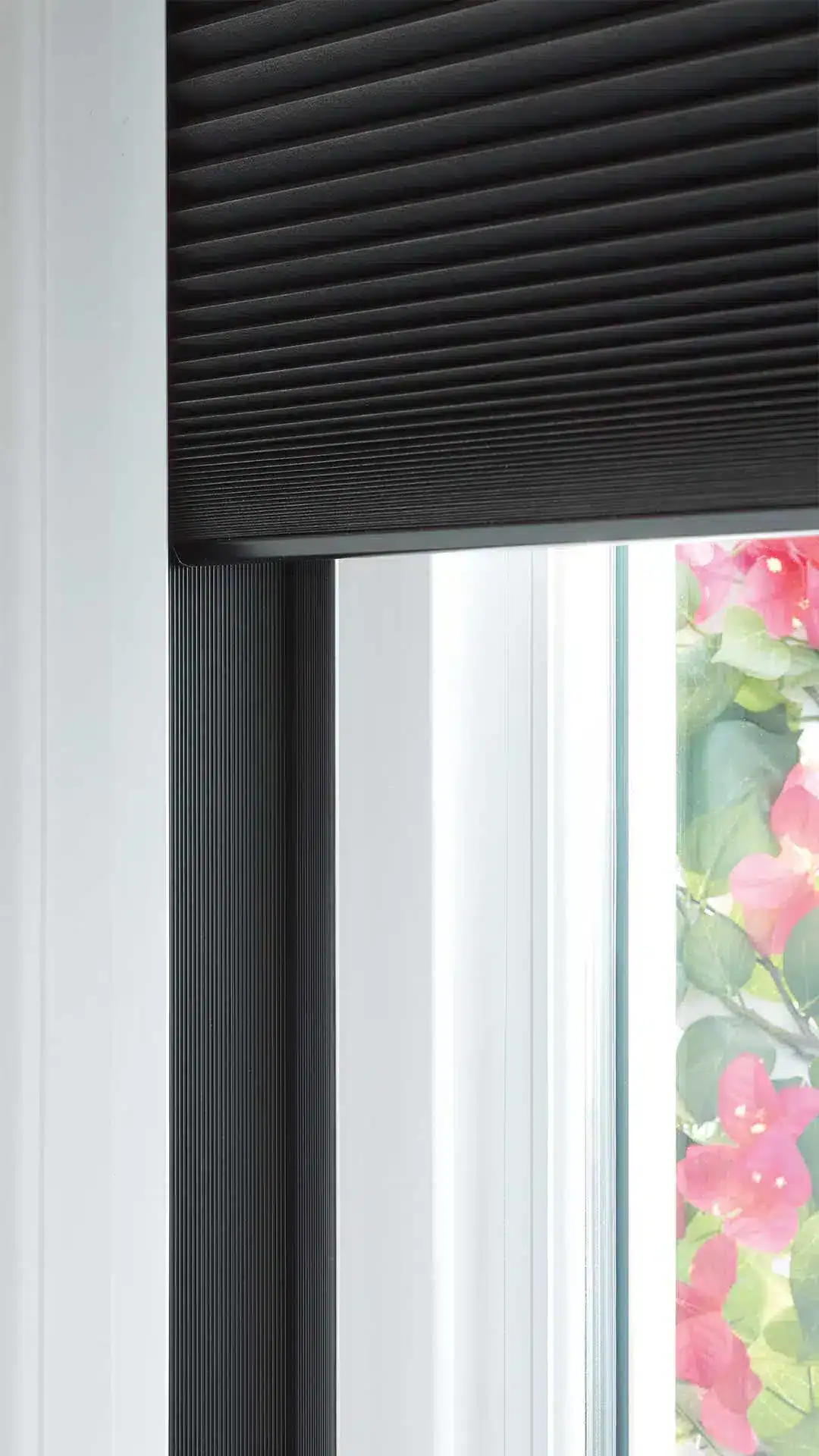 A close-up of a window with modern black ribbed blinds, allowing light to filter through, with colorful bougainvillaea flowers outside, creating a bright, stylish, and inviting atmosphere.