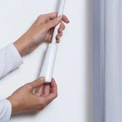 Hands installing a Powerview Automation Luminette system on a window, demonstrating smart window treatment technology.