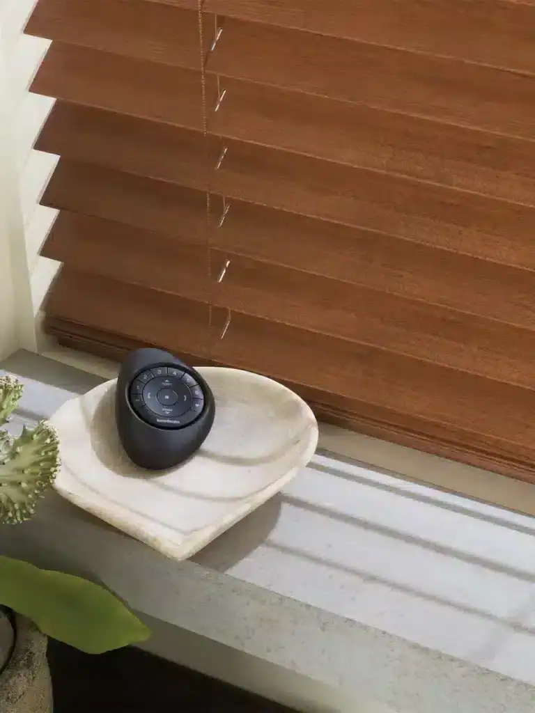 Elevated view of wooden window blinds with smart speaker on stone ledge, showcasing a blend of natural textures and smart home technology for a cozy, modern interior design.