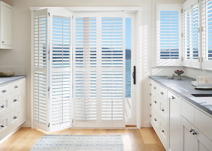Beautiful kitchen with large white plantation shutters overlooking water, bright natural light, modern cabinetry, and serene ocean views, perfect for beach house decor or coastal living.