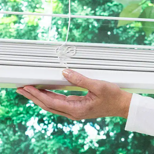 Close-up of hand opening a white sliding glass door with a green outdoor view.