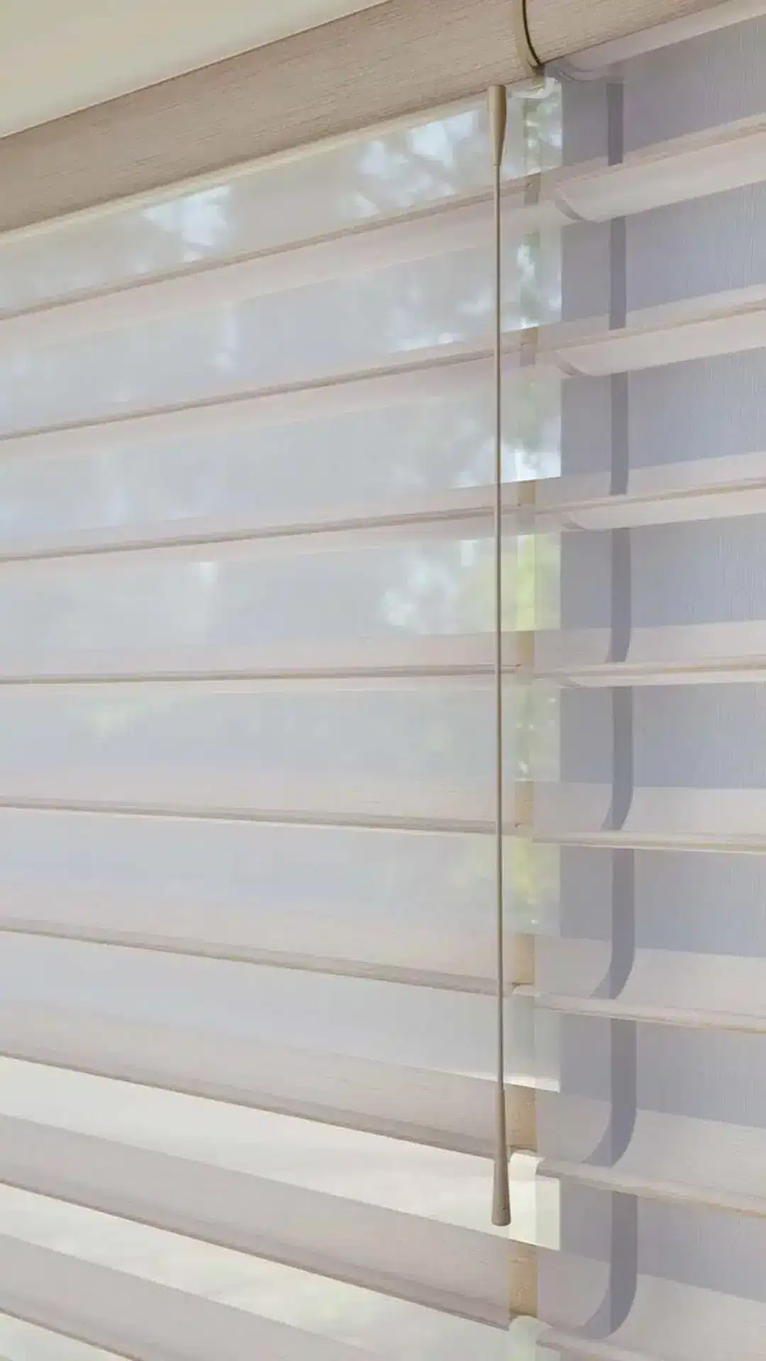 Modern beige window blinds with a pull cord on a white window frame, allowing adjustable sunlight filtering for privacy and room lighting.