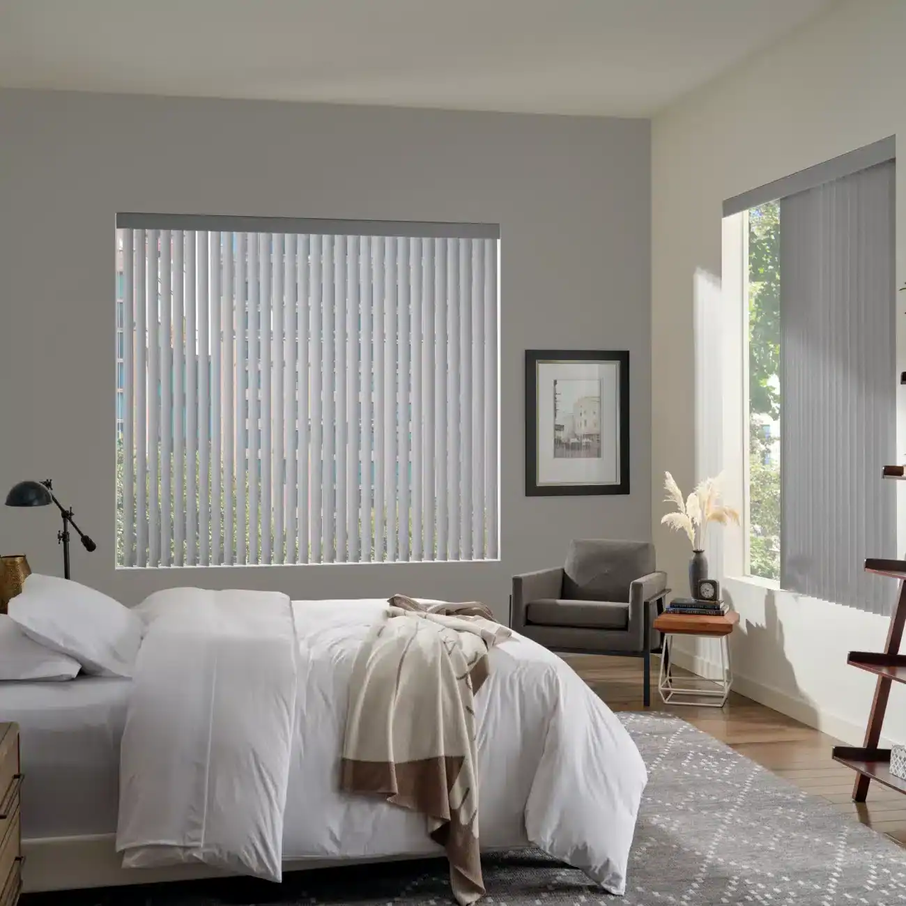 Spacious bedroom with large windows and vertical blinds, soft bedding, modern decor, and natural sunlight, creating a calm, relaxing environment ideal for contemporary living spaces.