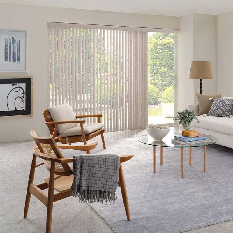 Bright and airy living room with minimalist decor, large window with vertical blinds, cozy seating with wooden chairs and a neutral color palette, perfect for relaxation and entertaining.