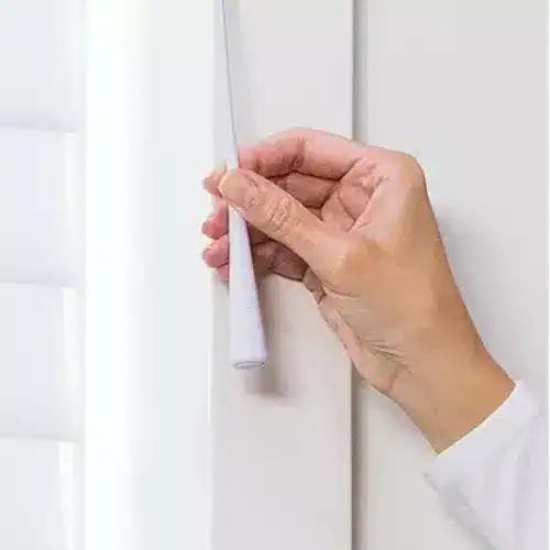 Close-up of a hand installing or adjusting a white roller window blind on a modern white wall, emphasizing home decor, window coverings, and interior design.
