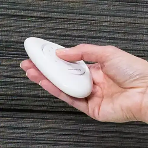 A hand holding a white remote control with buttons, used for operating electronic devices.