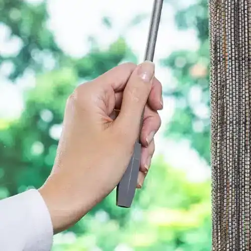 Close-up of a hand holding a window squeegee cleaning a beaded curtain, with a blurred green outdoor background emphasizing cleanliness and home maintenance.