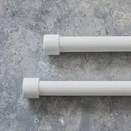 Two white curtain rods lying parallel on a gray marble-like surface.