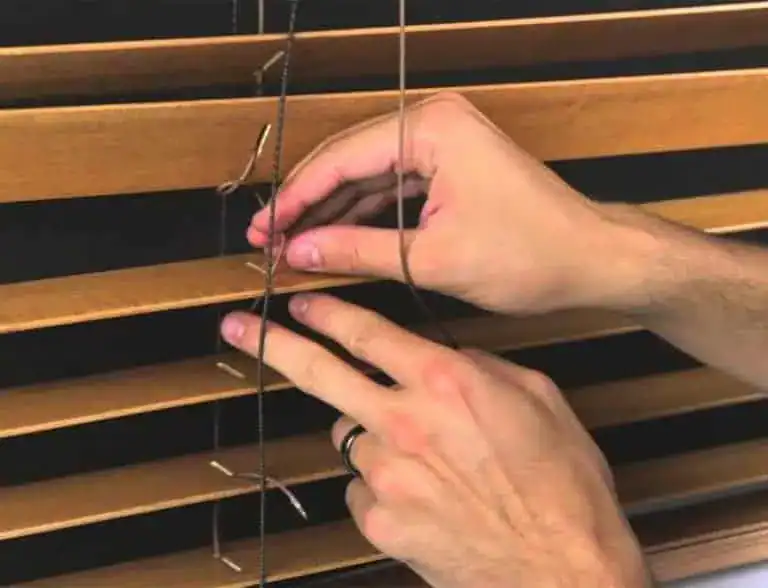 Close-up of hands fixing wooden window blinds with a small tool.