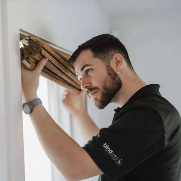 A man installing wooden window blinds, showcasing quality window coverings for home decor.