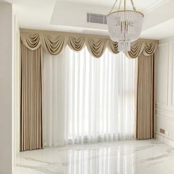 Luxurious beige draperies with valance and sheer curtains in a bright, modern room with chandelier and marble flooring.