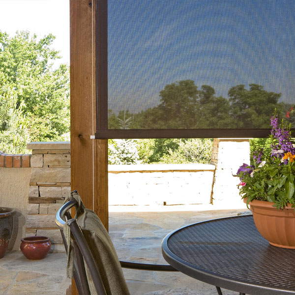 View of an outdoor patio with a round table, potted flowers, and a retractable screen with a scenic view of trees and blue sky.