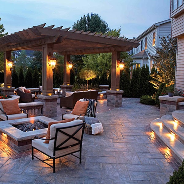 Elegant outdoor patio with warm lighting, cozy seating, and a pergola in a residential backyard at dusk.