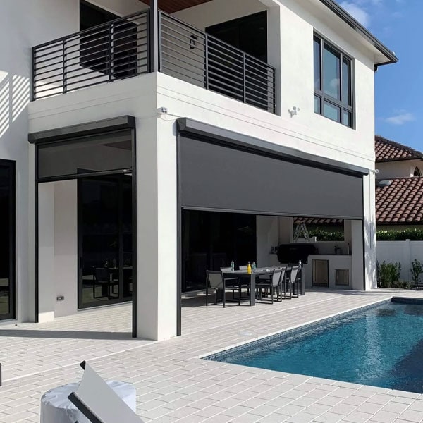 Contemporary two-story house with large glass windows, balcony, and a patio with a retractable awning over the outdoor dining area.