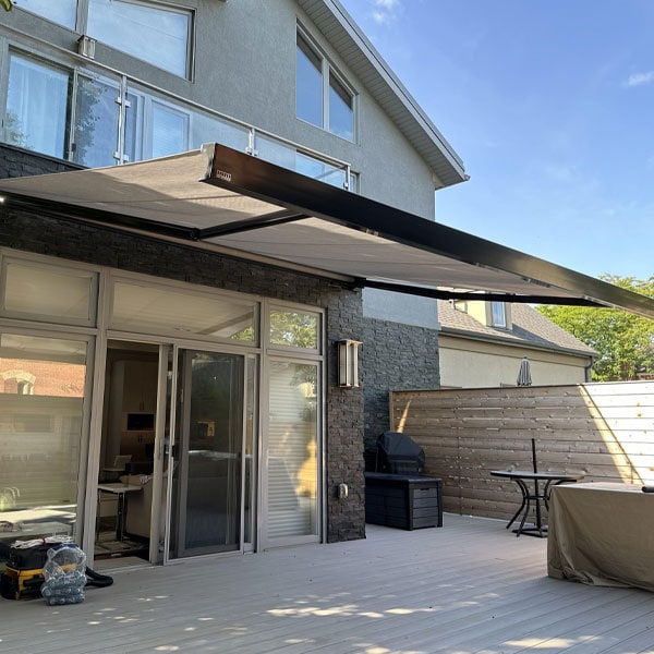 Large black retractable awning extending over a backyard patio with outdoor furniture and a wooden privacy fence.